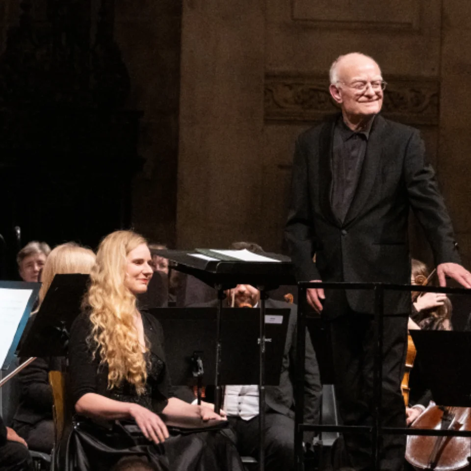 John Rutter smiling and facing the audience on the conductor's podium