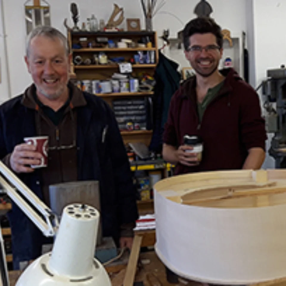 2 men holding coffee in front of a Double Bass that is being built
