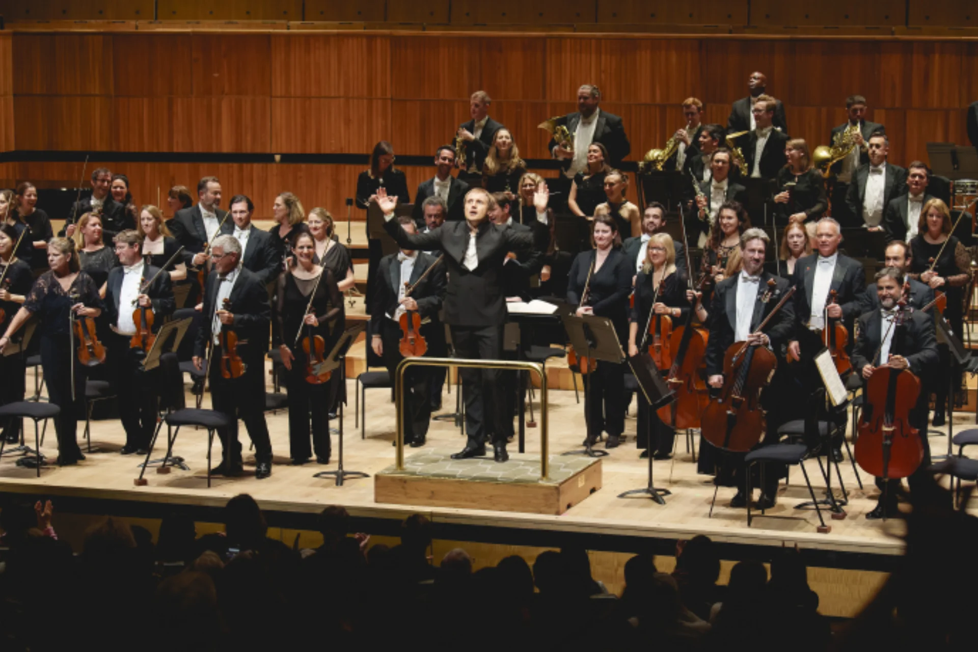 Orchestra and conductor standing up in front of an audience
