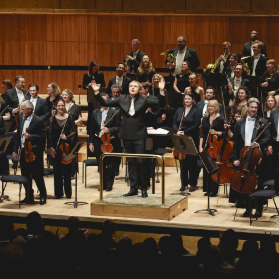 Orchestra and conductor standing up in front of an audience