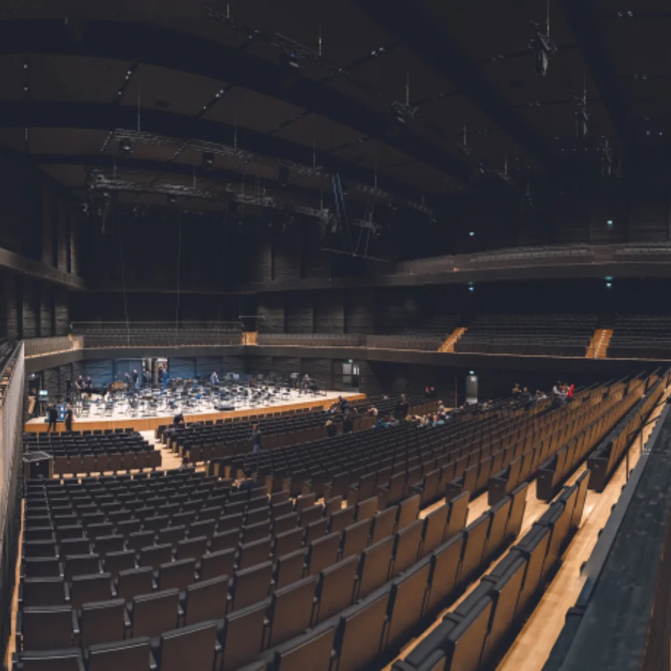 Orchestra playing in a large concert hall with 1 person in the audience