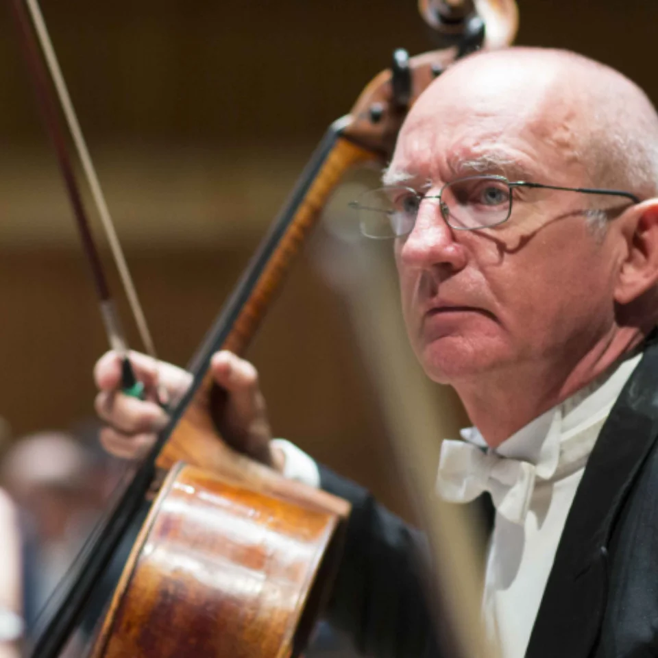 RPO Player William Heggart holding his cello in concert attire.